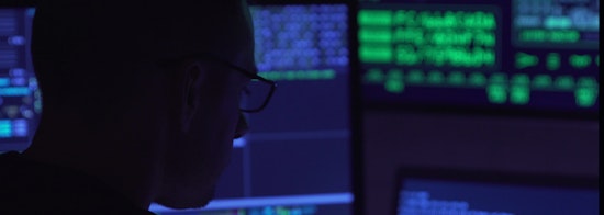 Man with glasses looking at multiple lit up computer screens 
