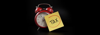 A sticky note saying tax leaning against a red alarm clock
