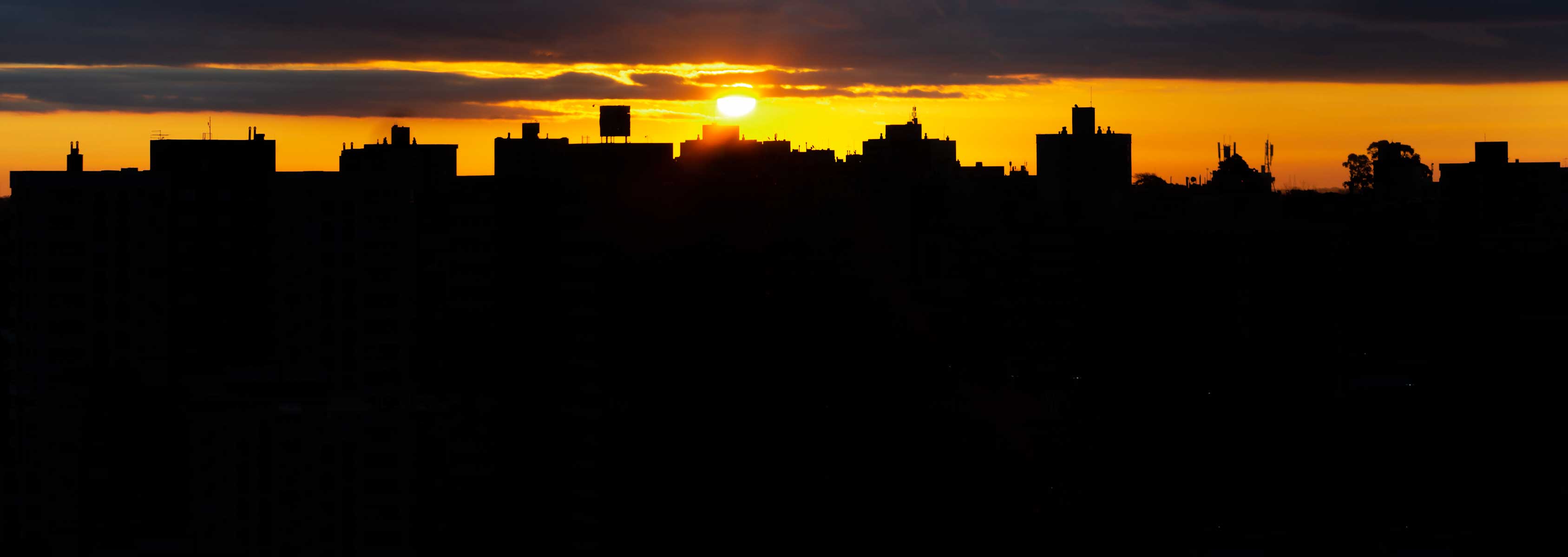 Sun rising behind an array of buildings. 